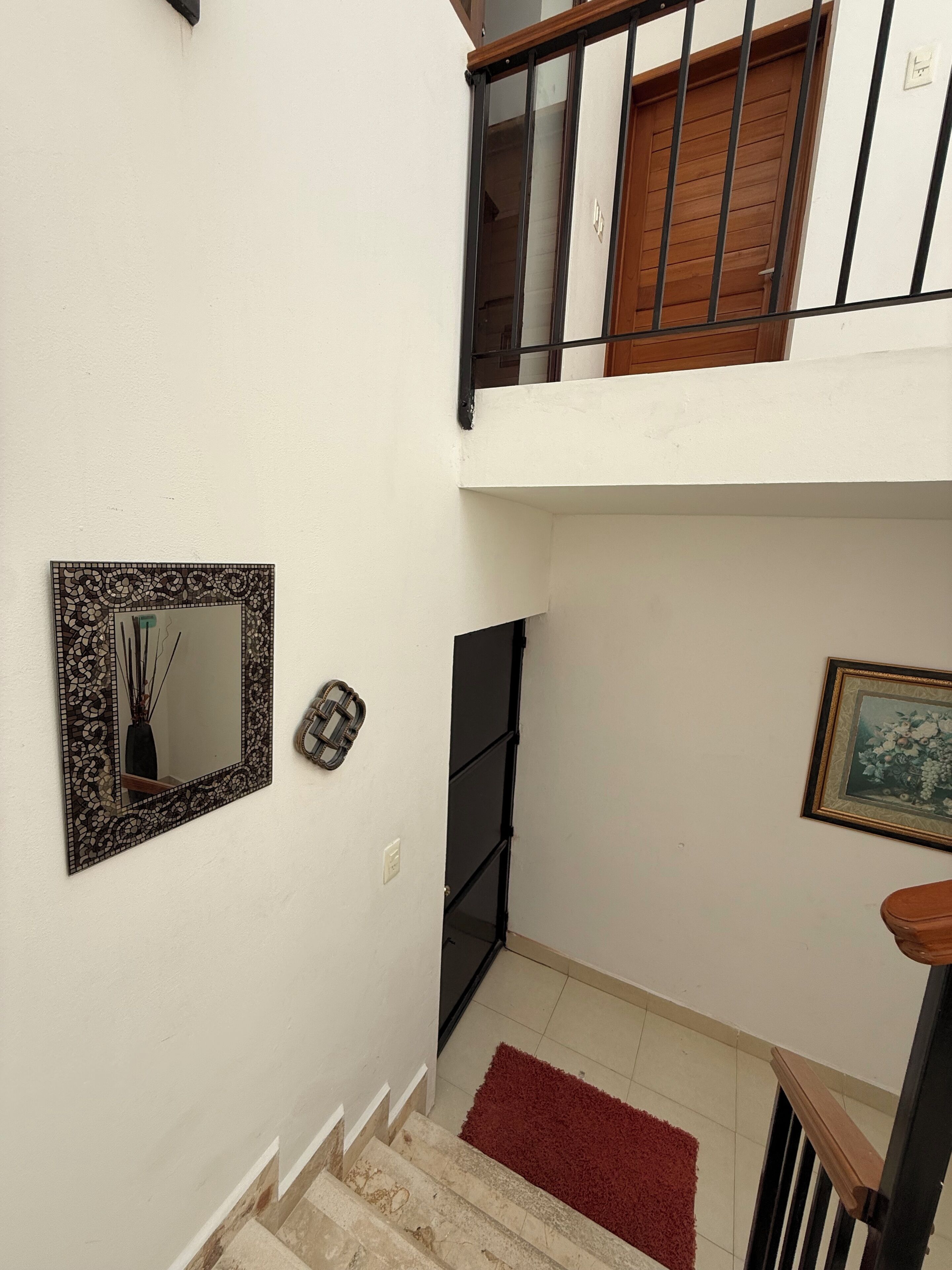 Un escalier recouvert d’un tapis rouge, un miroir encadré et un tableau accroché au mur.