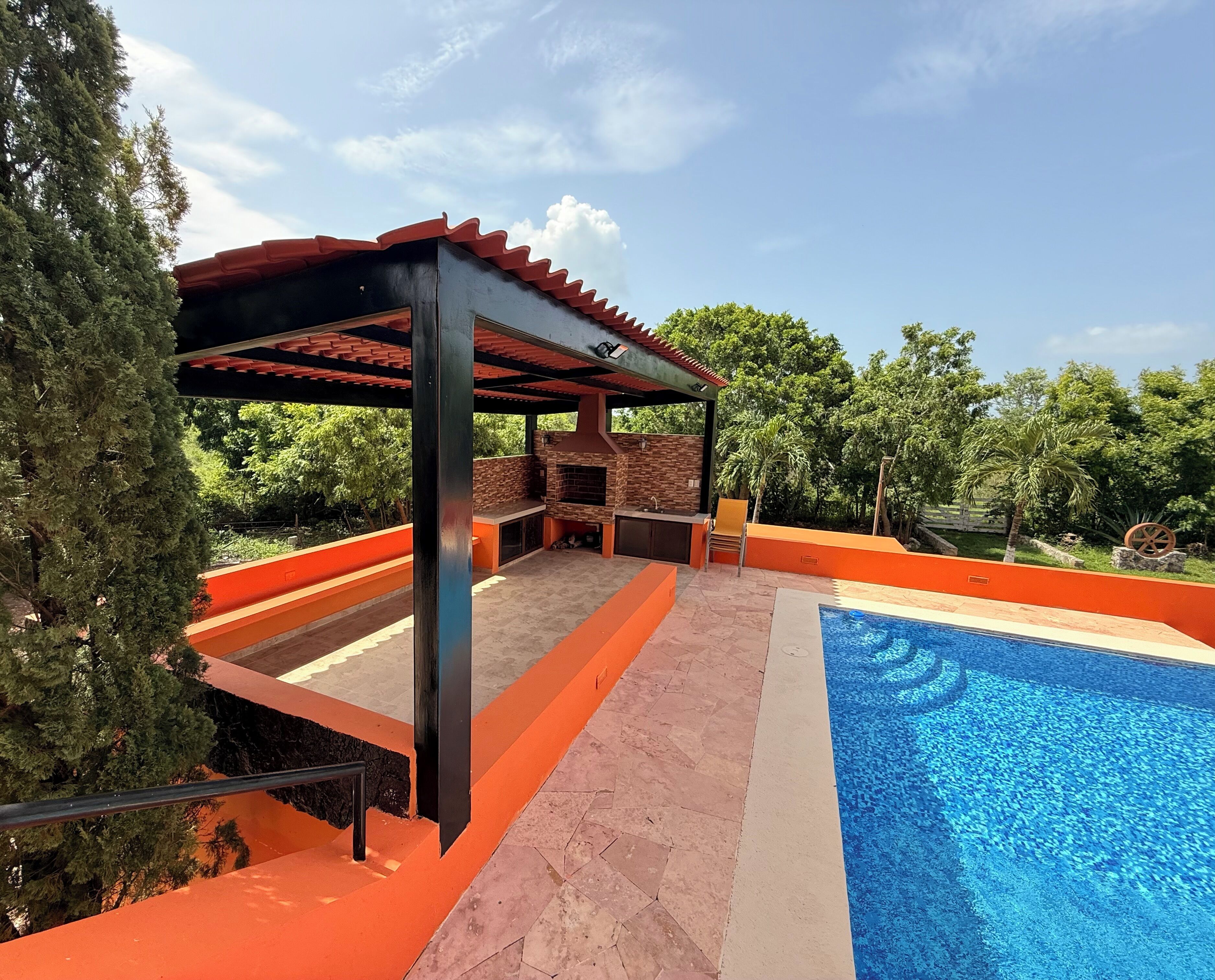 A covered outdoor area with a pool, stone barbecue, and orange accents.
