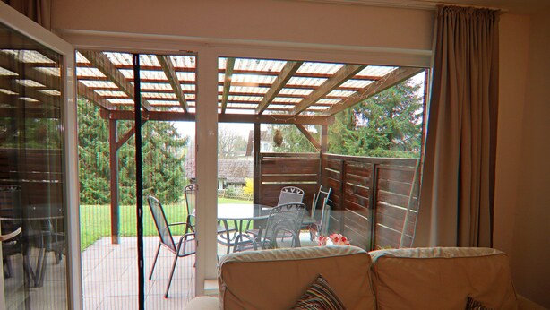 A cozy living room with a sofa, a glass door leading to a patio, and a wooden deck. - Apartment in Braunlage (Braunlage)