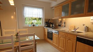A kitchen with wooden cabinets, a dishwasher, a stove, and a window with a view of greenery. - Apartment in Braunlage (Braunlage)