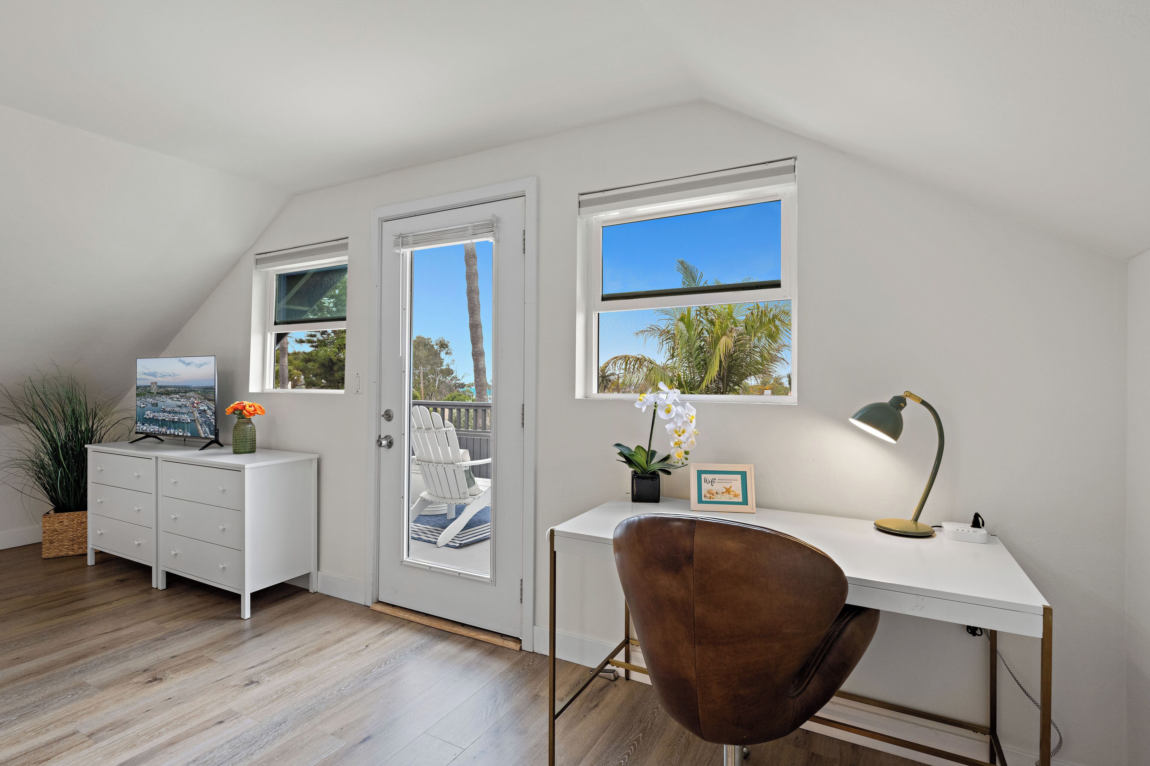 A modern, well-lit room with a white desk, brown chair, and a view of the outdoors through a large window.
