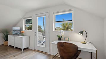 A modern, well-lit room with a white desk, brown chair, and a view of the outdoors through a large window.