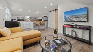 A modern living room with a sofa, a coffee table, and a TV displaying a beach view. - Ocean-View 1BR Retreat w/ Large Private Terrace - Walk to Beach & Dining (Solana Beach)