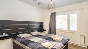Un dormitorio moderno con una cama grande, una mesita de noche, una lámpara de pared y un ventanal con cortinas.
