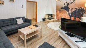 Una sala de estar moderna con sofá, mesa de centro, televisor, chimenea y un gran mural de un ciervo.