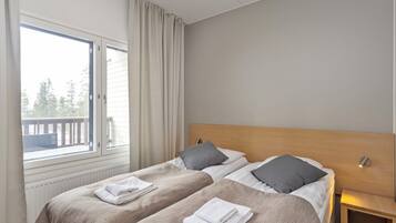 A hotel room with two beds, a window with curtains, a wooden headboard, and a bedside table with a lamp.