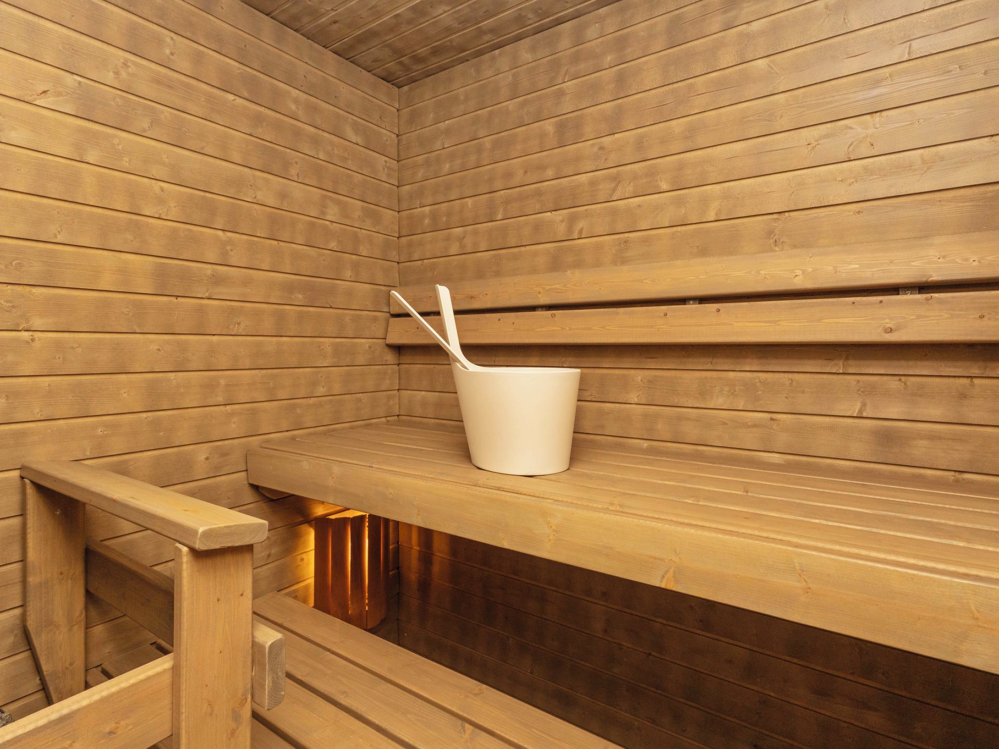 Un sauna en bois avec des bancs et un seau blanc muni d’une louche.
