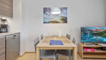 A modern kitchen with a coffee machine, a dining table with chairs, a painting, and a television.