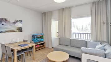 A modern living room with a sofa, a television, a dining table with chairs, and a window with curtains.
