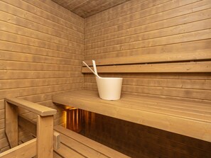 A sauna room with wooden benches and a white bucket with a spoon.
