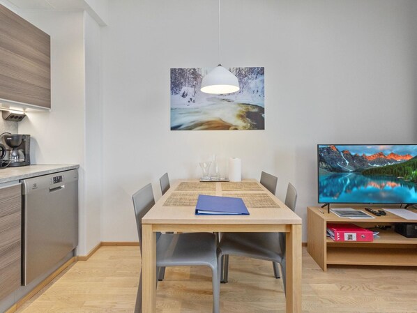 A modern kitchen with a dishwasher, a coffee machine, and a dining area with a wooden table and chairs.
