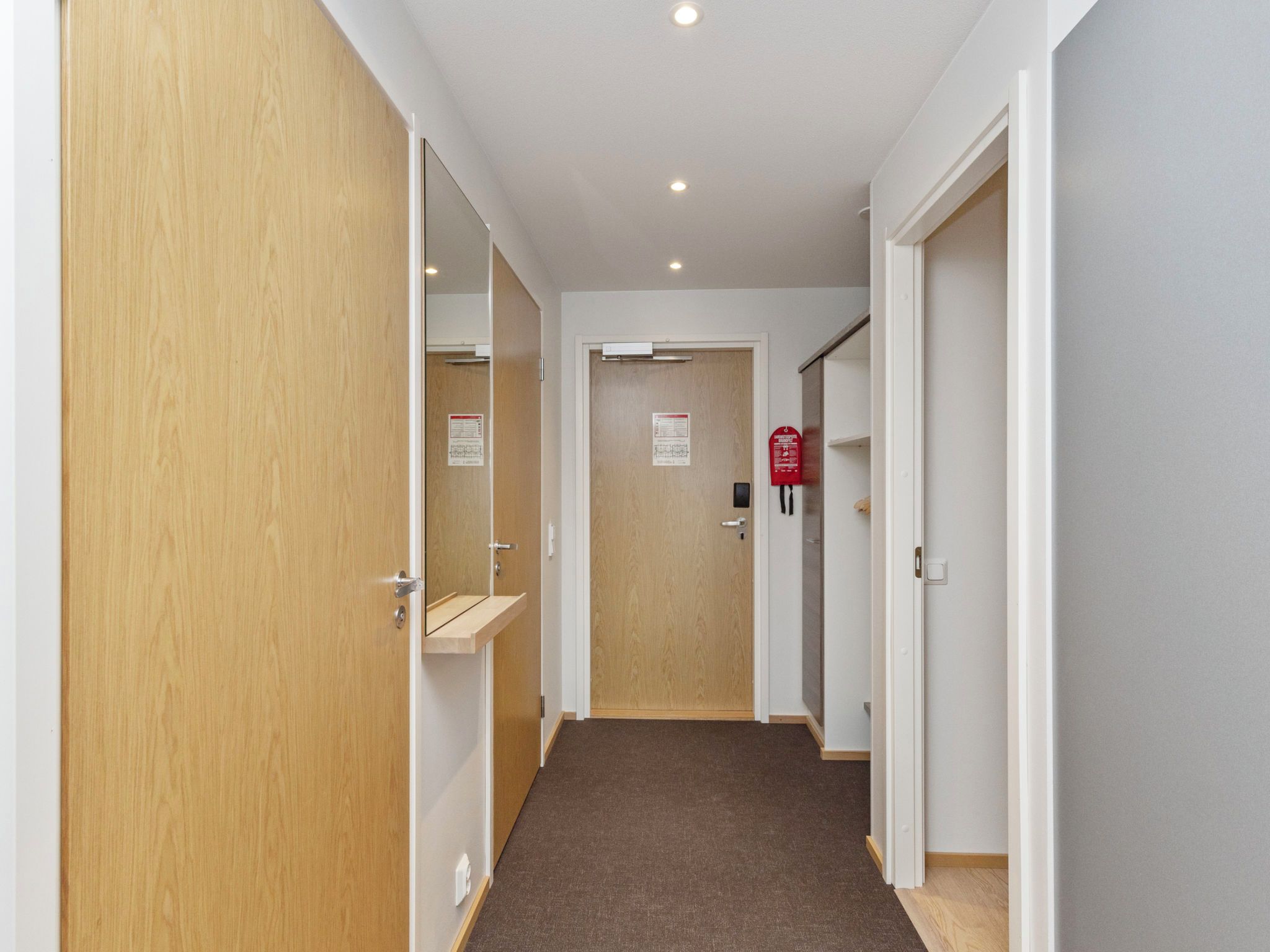 A hallway with wooden doors, a fire alarm, and a carpeted floor.
