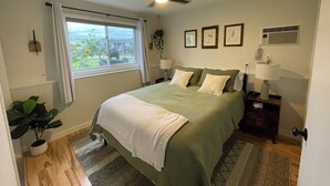Ein Schlafzimmer mit Bett, Deckenventilator, Fenster, Pflanze und Wandlampe.
