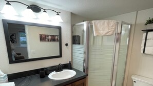 Ein Badezimmer mit einem Holzlagerfläschchen, einem weißen Waschbecken, einem Spiegel und einer Duschkabine aus Glas.