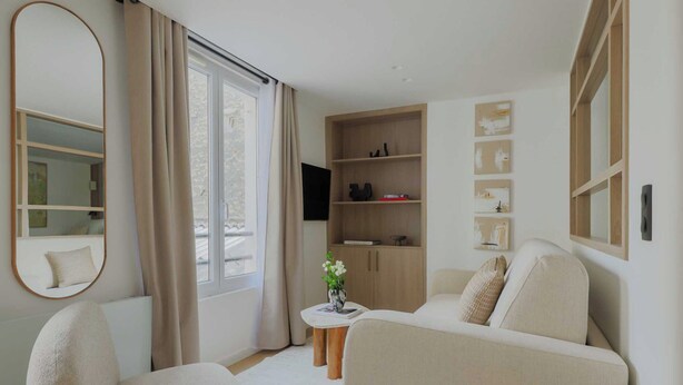 Un salon moderne comprenant un canapé, des fauteuils, une table basse, une table d’appoint avec un vase, une bibliothèque et un grand miroir.