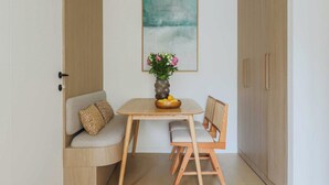 Une pièce de taille modeste, avec un meuble en bois, un canapé agrémenté d’un coussin à motifs, une petite table sur laquelle sont posés un vase et un panier de fruits, et une œuvre d’art encadrée accrochée au mur.
