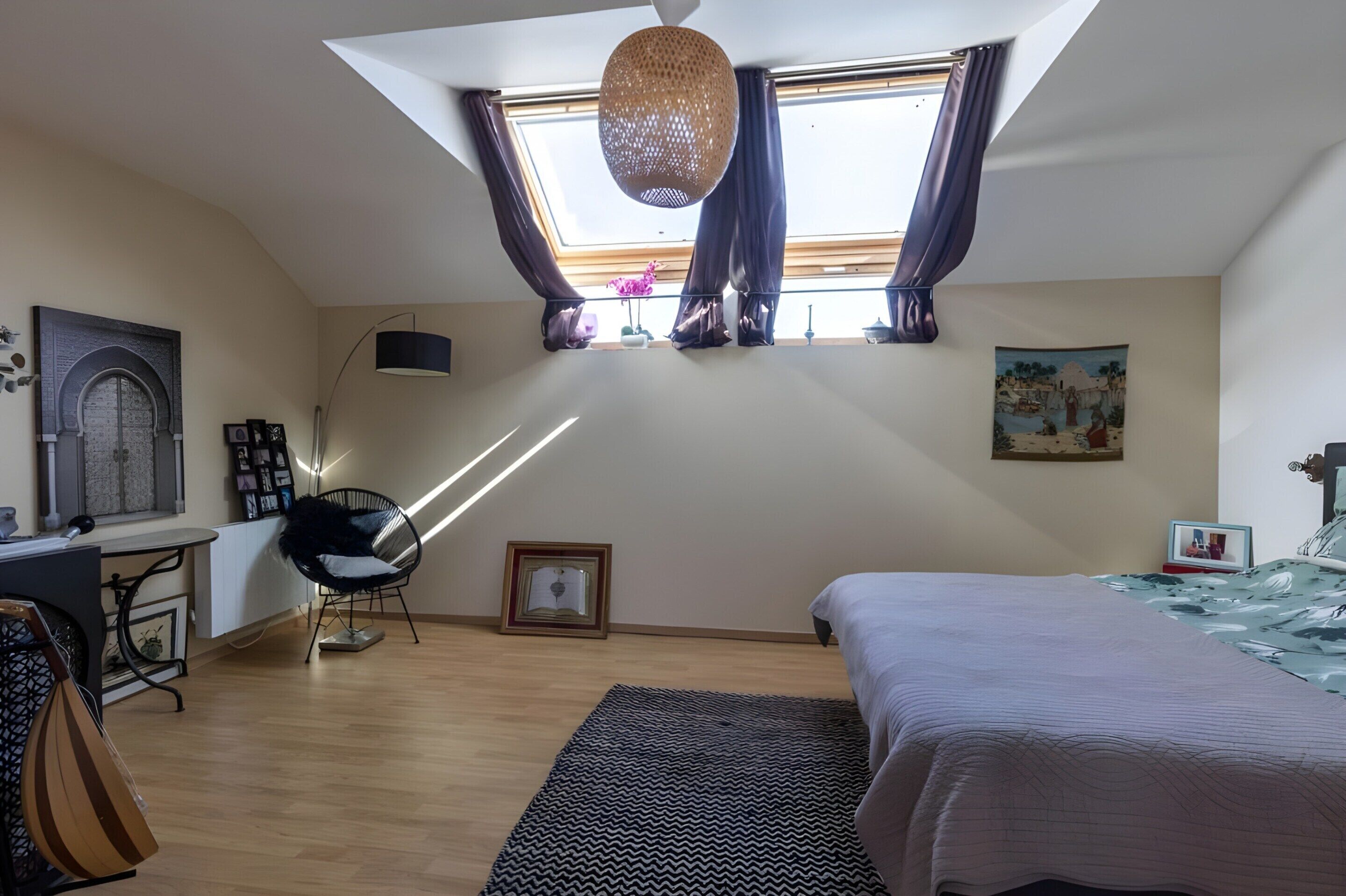 A bedroom with a skylight, a bed, a desk with a chair, a bookshelf, and a wall-mounted lamp.