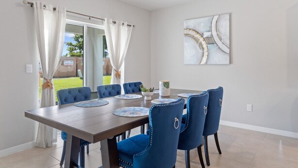Een eethoek met een rechthoekige tafel, zes blauwe fauteuils en een modern abstract schilderij aan de muur.