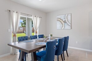 Ein Essbereich mit einem rechteckigen Tisch, sechs blauen Polsterstühlen und einem modernen, abstrakten Gemälde an der Wand.