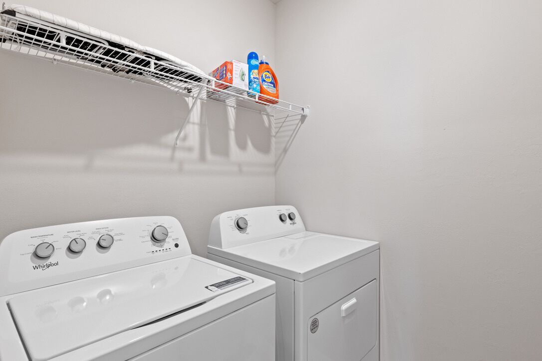 A laundry area with two white Whirlpool washers and a drying rack.