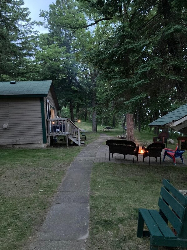 A wooden cabin with a porch and a fire pit area with benches.