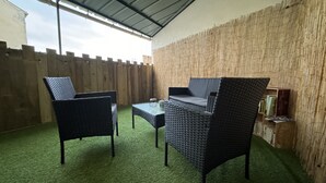 Eine Terrasse im Freien mit Korbmöbeln, einem Tisch und einem Bücherregal an einer Bambuswand.