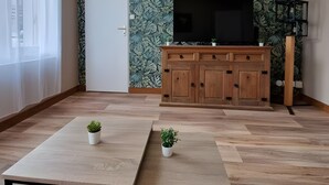 Ein Wohnzimmer mit Holzboden, einem Fernseher auf einer Holzkommode und zwei kleinen Topfpflanzen.
