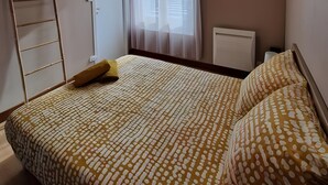 Ein Schlafzimmer mit einem Bett, einer Leiter, einer Tür und einem Fenster mit Vorhängen.