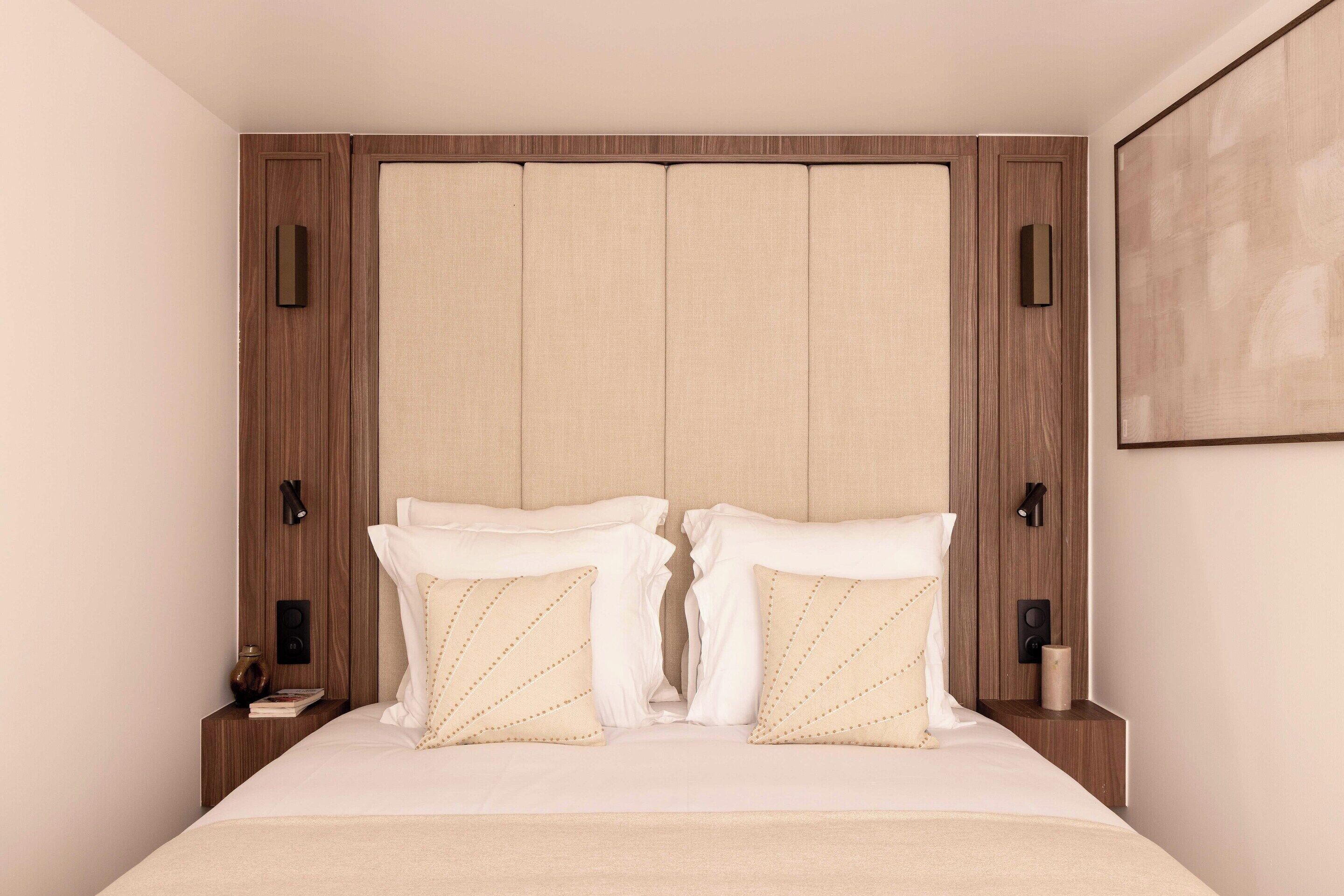 A bedroom with a large bed, wooden headboard, two bedside tables, and a wall-mounted artwork.