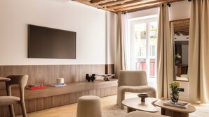 Una habitación de hotel moderna con una pared decorativa de madera, un televisor de pantalla plana, una zona de estar acogedora con un sofá y sillones, una mesita de centro pequeña y una mesita auxiliar con un florero.