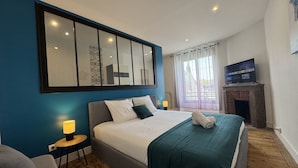 Een moderne hotelkamer met een groot bed, een klein tafeltje met een lamp, een televisie en een open haard.