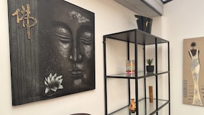 Een modern interieur met een donker abstract schilderij, een houten bijzettafeltje en een metalen open kast met diverse spullen.