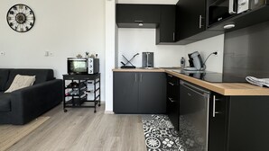 Una cocina moderna con armarios negros, un microondas y una cafetera. En la sala de estar, hay un sofá negro con un cojín estampado.