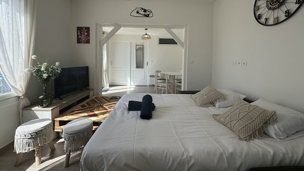 Un dormitorio con una cama grande, televisión, escritorio y una silla. Hay una puerta que conduce a otra habitación.