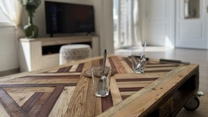 Una mesa de madera con un diseño geométrico, un vaso con una cuchara y un televisor al fondo.