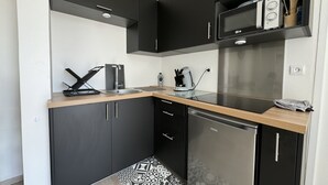 Una cocina compacta con armarios oscuros, un microondas de acero inoxidable, una cafetera y un lavavajillas.