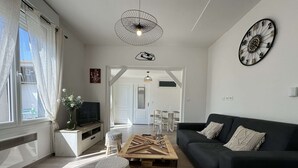 Una sala de estar moderna con un sofá negro, una mesa de centro de madera, un televisor sobre un soporte blanco, un reloj de pared decorativo y un ventilador de techo.
