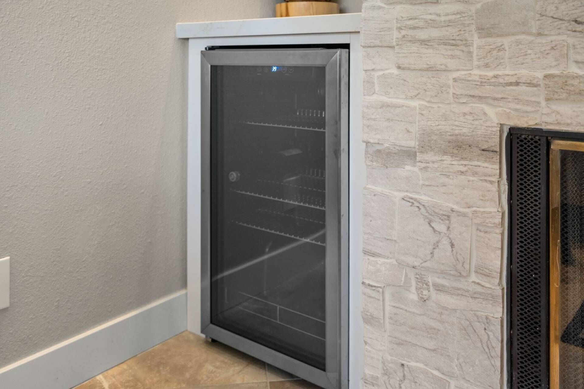 A corner of a room with a built-in wine cooler, stone wall, and a tiled floor.