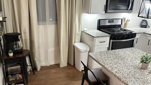 Una cocina compacta con armarios blancos, microondas, estufa y encimera de granito.