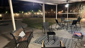 Un patio al aire libre con un muro de piedra, césped y una zona de estar que incluye un banco y sillas.