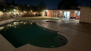 Una piscina de diseño curvo, rodeada por una zona de patio con mobiliario exterior y un edificio de ladrillo al fondo.