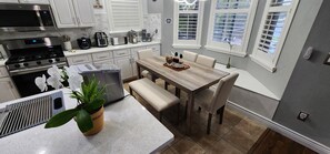 A modern kitchen with stainless steel appliances, a dining area with a wooden table and chairs, and a potted plant on the counter.