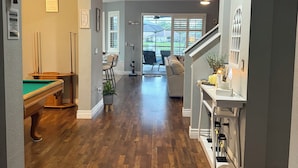 A hallway with a pool table, a staircase, and a view to the outside. - Relax in my calm and stylish space. Enjoy the relaxing lakeview and heated pool. (Riverview)