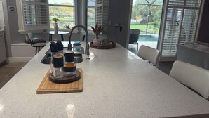 A kitchen with a large island, a sink, and a view of a backyard through the windows. - Relax in my calm and stylish space. Enjoy the relaxing lakeview and heated pool. (Riverview)