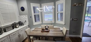A kitchen with white cabinets, a wooden dining table, and a window with blinds.