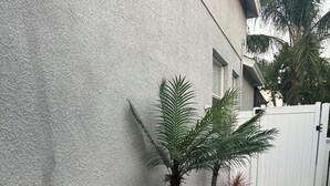 A pathway lined with white pebbles and palm trees, leading to a white gate. - Relax in my calm and stylish space. Enjoy the relaxing lakeview and heated pool. (Riverview)
