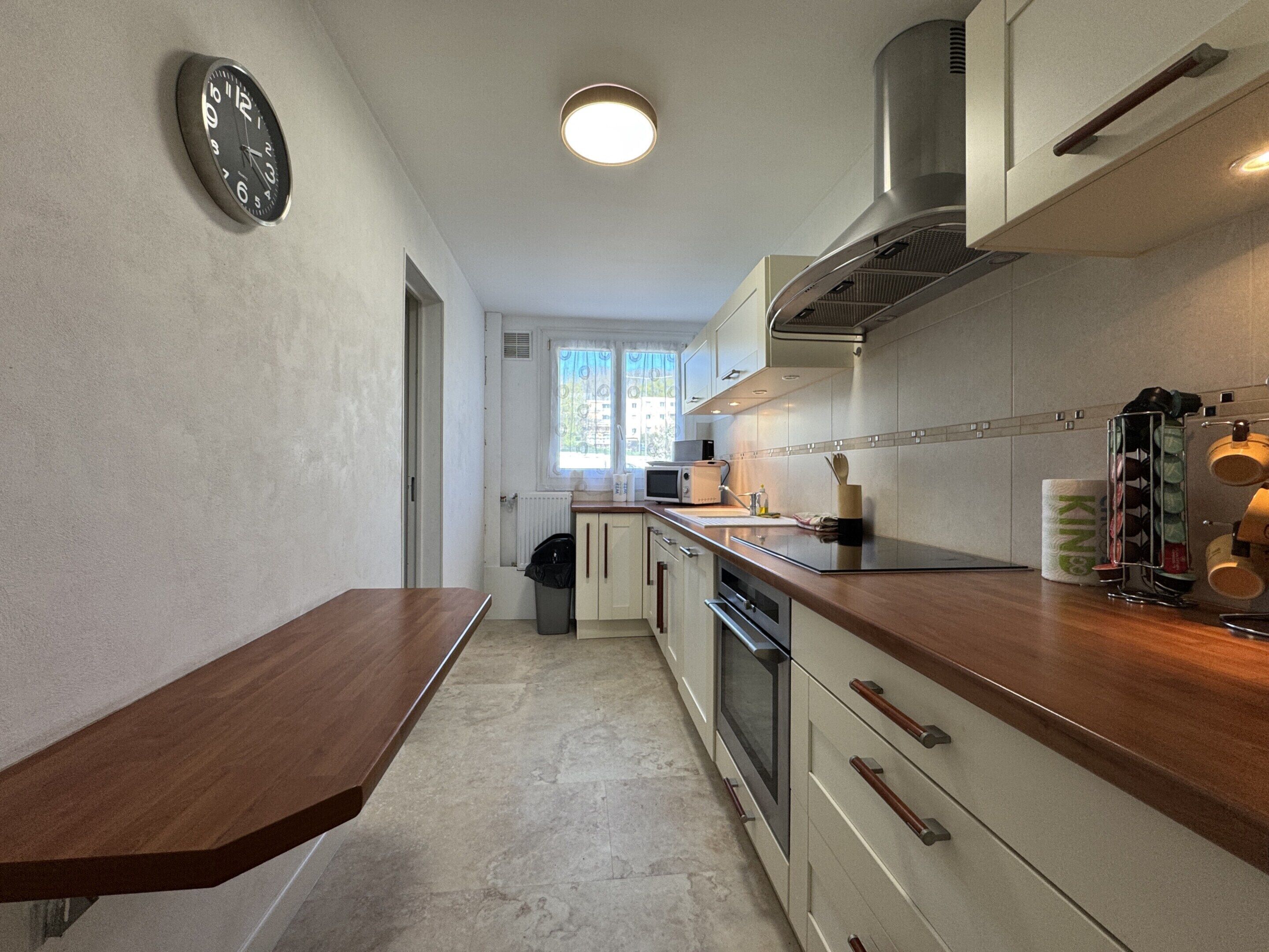 A modern kitchen with a wooden countertop, stainless steel appliances, and a clock on the wall.