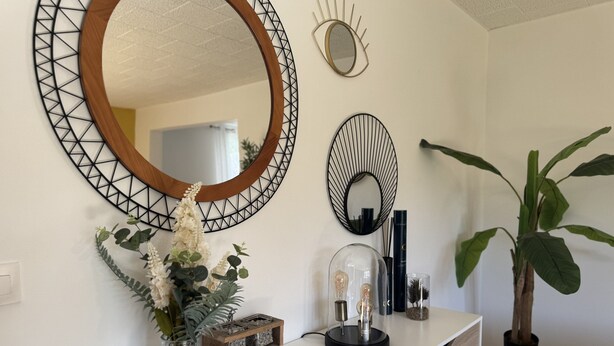 A modern interior with a white vanity, a large mirror, decorative wall art, a potted plant, and a small wooden shelf with decorative items.