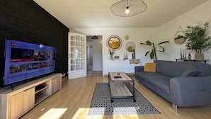 A modern living room with a flat-screen TV, a grey sofa, a coffee table, and a patterned rug.