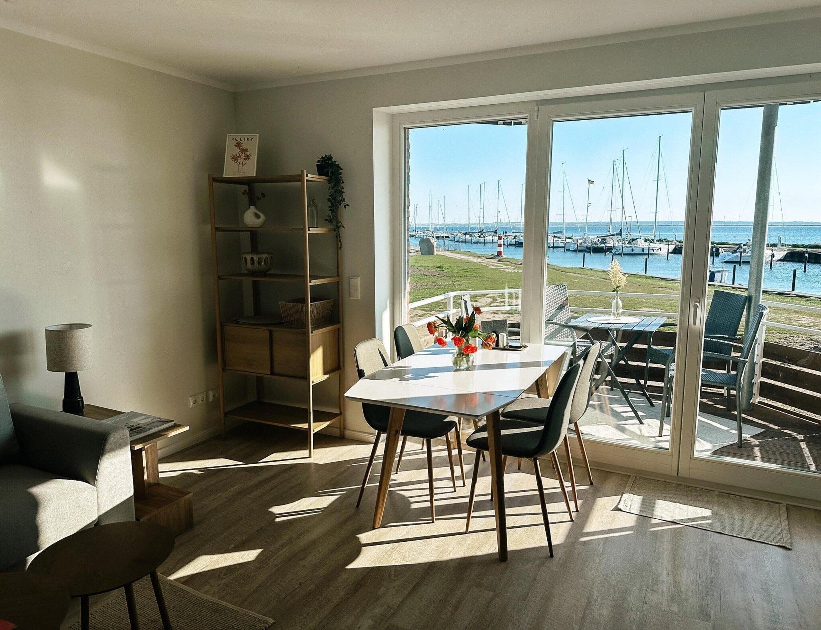 A dining area with a view of a marina, a bookshelf, and a lamp.